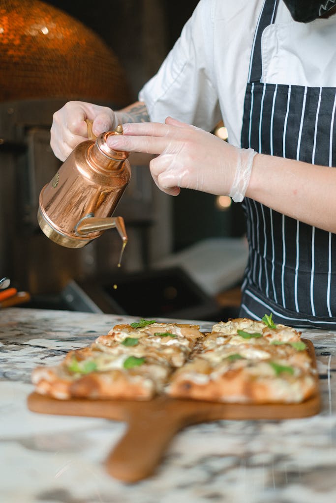 A chef drizzles olive oil on a freshly prepared gourmet pizza, enhancing its flavor and presentation.