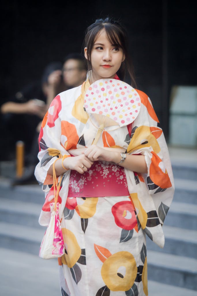 A young woman wearing a colorful floral kimono and holding a fan, embodying traditional Japanese fashion.