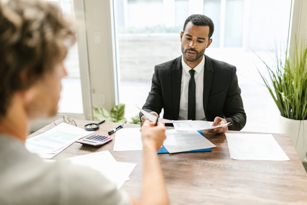 Businessman in a suit reviewing documents during a meeting indoors with a colleague.